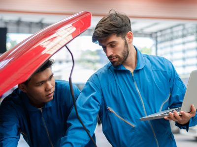 Car mechanic team using laptop boosting car engine at auto repair shop