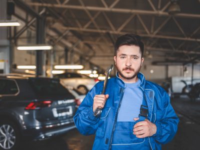 Portrait of a car mechanic who holds wrench on his shoulder. Auto mechanic in the garage